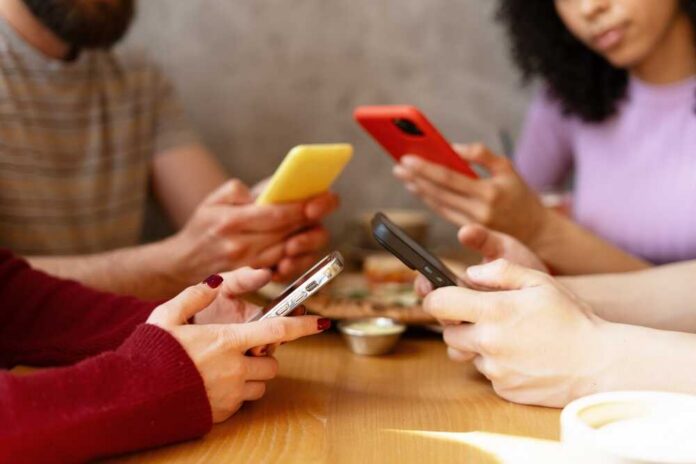 Group of friends sitting at a table, each using their smartphones
