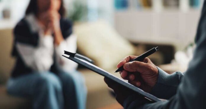 A therapist taking notes during a session with a client in the background