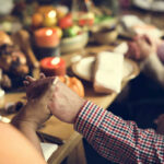 Two hands holding each other over a festive dinner table with candles and food