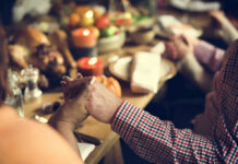 Two hands holding each other over a festive dinner table with candles and food