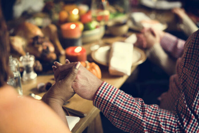 Two hands holding each other over a festive dinner table with candles and food