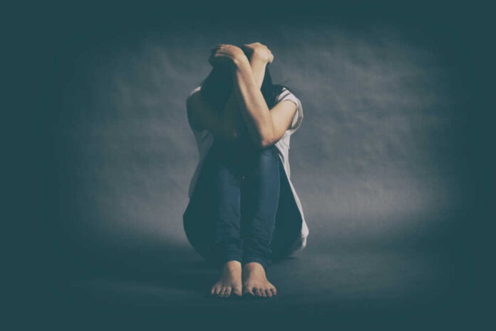 A person sitting on the floor with their arms wrapped around their knees, conveying a sense of distress