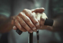 Close-up of elderly hands resting on a walking cane