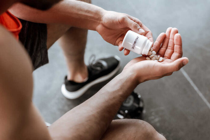 Cropped,View,Of,Sportsman,Holding,Bottle,With,Probiotic,Lettering,And Person pouring probiotic pills into their hand