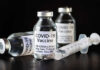 Vials of COVID-19 vaccine and a syringe on a dark background