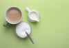 A cup of coffee, a bowl of sugar, and a creamer on a green background