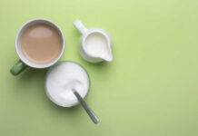 A cup of coffee, a bowl of sugar, and a creamer on a green background