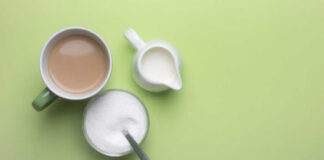 A cup of coffee, a bowl of sugar, and a creamer on a green background