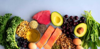 An assortment of healthy foods including fish, nuts, fruits, and vegetables arranged on a light background