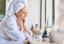 The 5-10 Shave Myth Woman in a bathrobe with a towel on her head, smiling at her reflection in a mirror