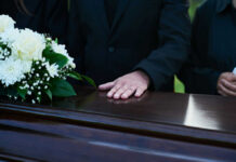 Forgotten Grievers: Sibling Loss Unseen Trauma A hand resting on a coffin adorned with white flowers during a funeral
