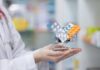 A doctor holding a miniature shopping cart filled with various medication packs