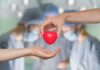 Two hands exchanging a red heart symbol in a surgical setting