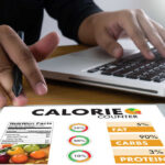 The Reason Your Healthy Eating Plans Often Fail Person using a calorie counter app on a tablet while working on a laptop