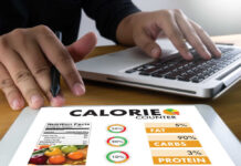 The Reason Your Healthy Eating Plans Often Fail Person using a calorie counter app on a tablet while working on a laptop