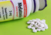 Bottle of melatonin tablets with some pills spilled on a green surface