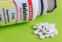 Bottle of melatonin tablets with some pills spilled on a green surface