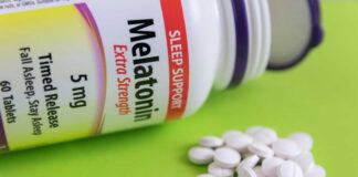 Bottle of melatonin tablets with some pills spilled on a green surface