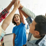 Group of children joyfully celebrating with high fives in a classroom