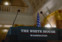 Press podium with microphones and an American flag in the background