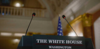 Press podium with microphones and an American flag in the background