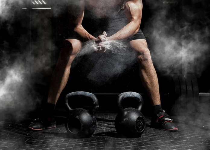 Weightlifter,Clapping,Hands,And,Preparing,For,Workout,At,A,Gym. Athlete preparing to lift kettlebells in a gym with chalk dust in the air