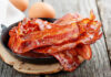 Crispy bacon strips in a cast iron skillet with eggs in the background