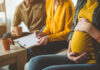 Oral Disease That Wrecks Fertility Timelines Pregnant woman sitting with two people discussing notes in a cozy living room