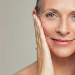 Close-up portrait of a smiling woman gently holding her face