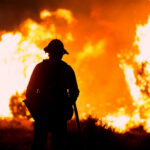 Silhouette of a firefighter standing in front of a large wildfire