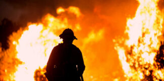 Silhouette of a firefighter standing in front of a large wildfire