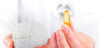 A medical professional holding a brain model in one hand and a yellow supplement capsule in the other