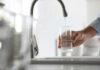 Nitrate in Tap Water May Raise Your Dementia Risk A hand holding a glass under a kitchen faucet while water is being poured into it