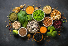 An assortment of legumes, nuts, and fresh vegetables arranged in bowls on a dark surface
