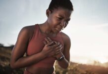The Best Exercise Sweet Spot For Your Heart Health A woman in athletic wear holding her chest with a pained expression outdoors