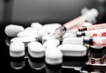 White pills and syringes arranged on a reflective surface