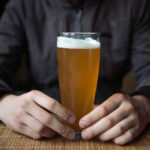 Early-Onset Cancer’s Hidden Accomplice Person holding a glass of craft beer in a bar