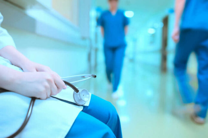 A healthcare professional holding a stethoscope in a hospital corridor