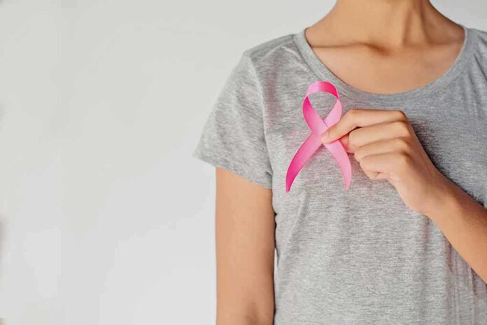 shutterstock_1032241918 Person holding a pink ribbon on a gray shirt