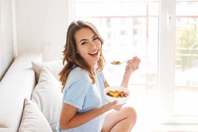 Woman sitting on a couch eating a bowl of fruit salad