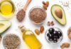 Plant Fats vs. Heart Attack Risk Assorted healthy fats with avocados, nuts, seeds, olives, and oils on a white background
