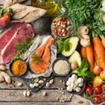 Assorted fresh ingredients with meat, salmon, fruits, and vegetables on a rustic table