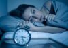 Woman lying awake in bed beside an alarm clock