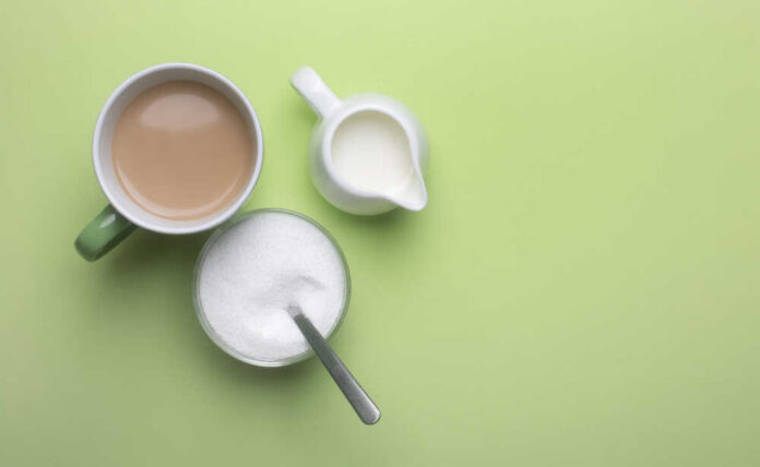 Coffee,In,A,Cup,With,Milk,With,A,Milk,Jug A cup of coffee, a bowl of sugar, and a creamer on a green background