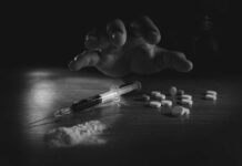 A hand reaching for pills next to a syringe and powder on a table