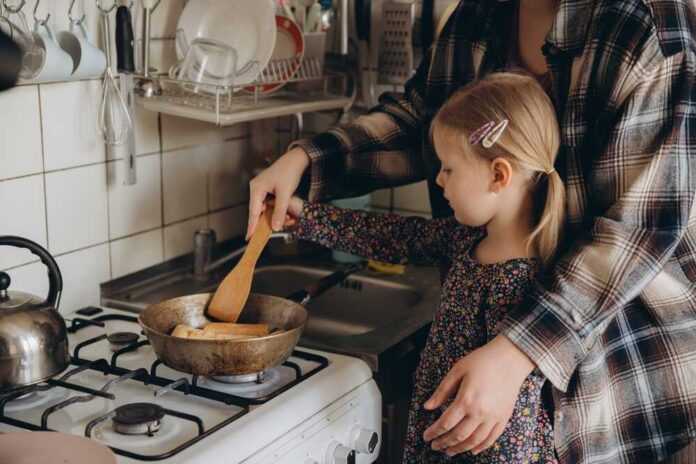 Parent,Standing,With,Child,In,Kitchen,,Teaching,Cooking,Skills.,Child Child cooking with adult at a stove