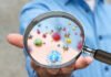 Anti-Cancer Treatment Found in Bacteria A person holding a magnifying glass showing colorful microorganisms