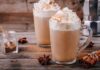 Two latte mugs with whipped cream and cinnamon on a rustic table