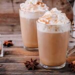 Two latte mugs with whipped cream and cinnamon on a rustic table