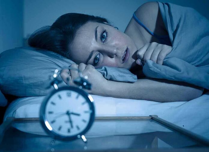 Woman lying awake in bed beside an alarm clock